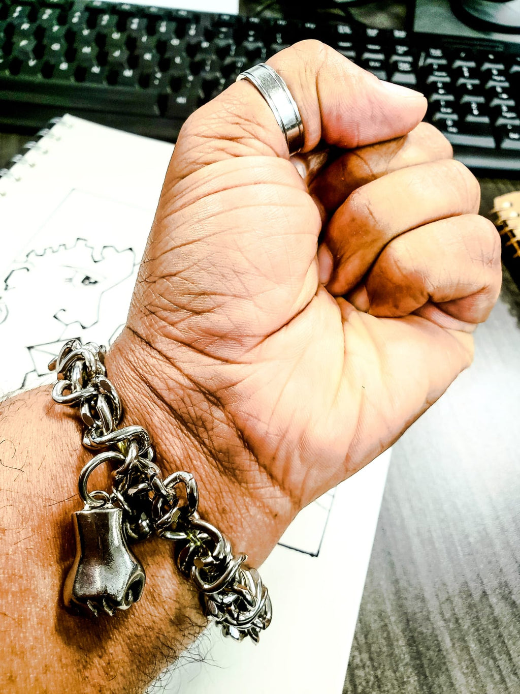 Hand wearing a silver bracelet with fist charm in front of a keyboard
