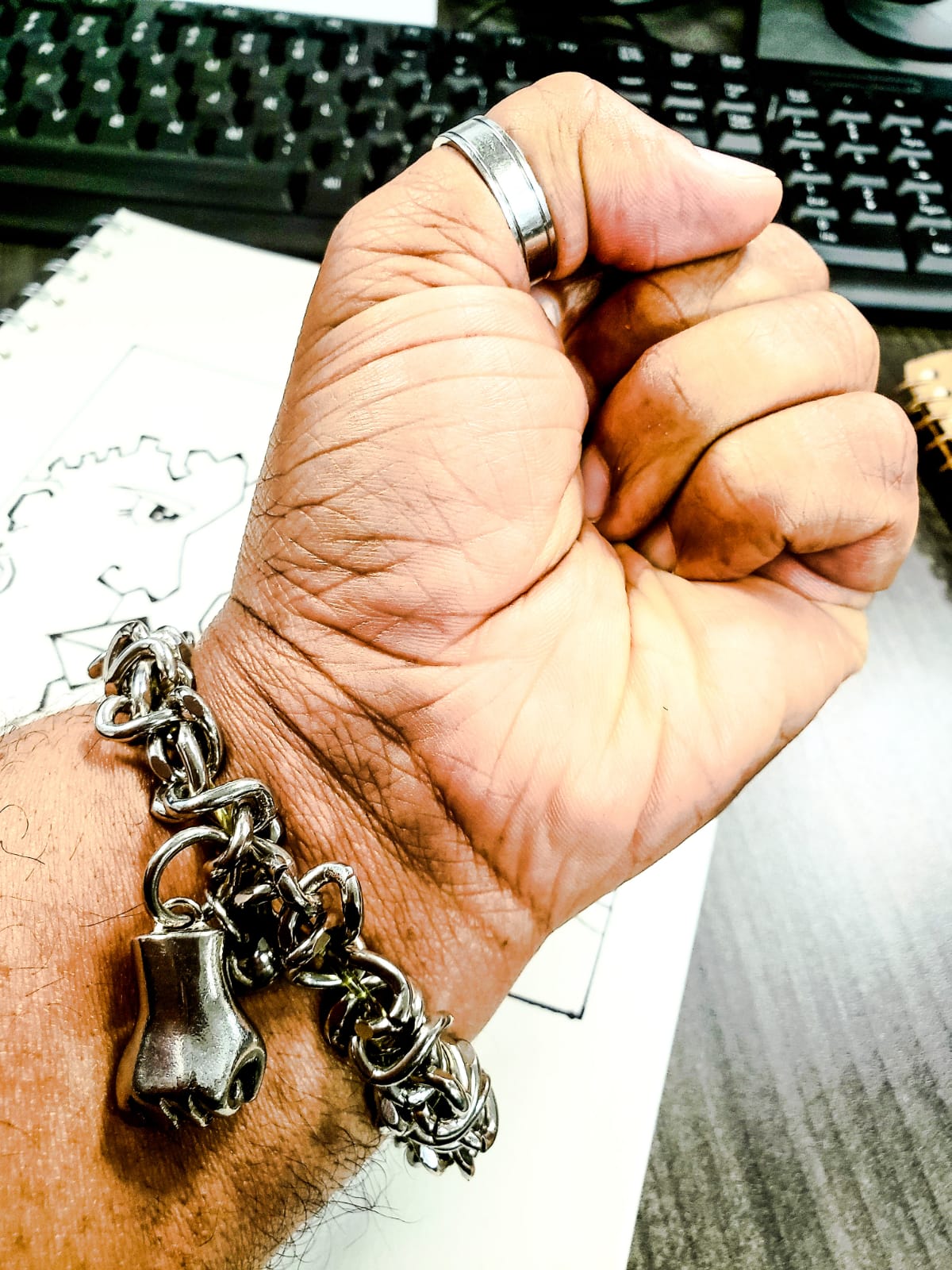 Hand wearing a silver bracelet with fist charm in front of a keyboard